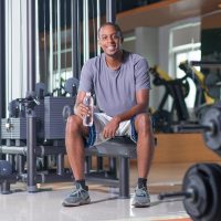 Smiling man sitting in gym, holding water bottle